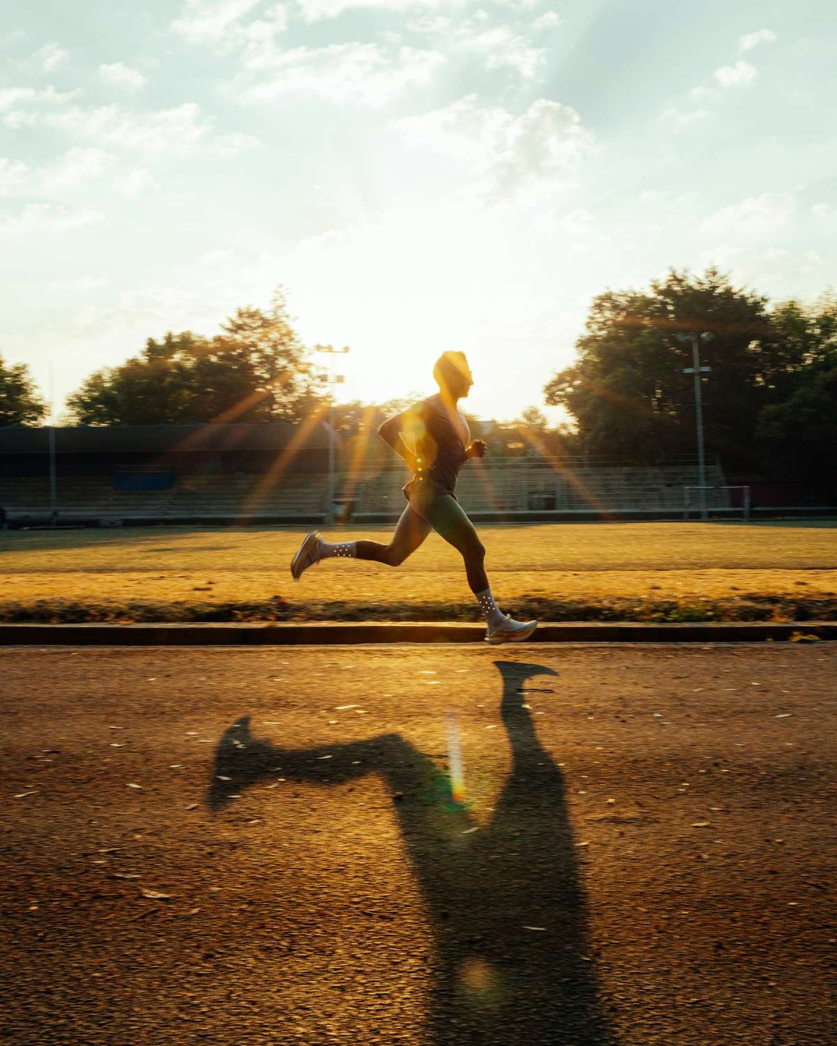Runner in side profile striding along a path at golden hour with sun flare behind trees