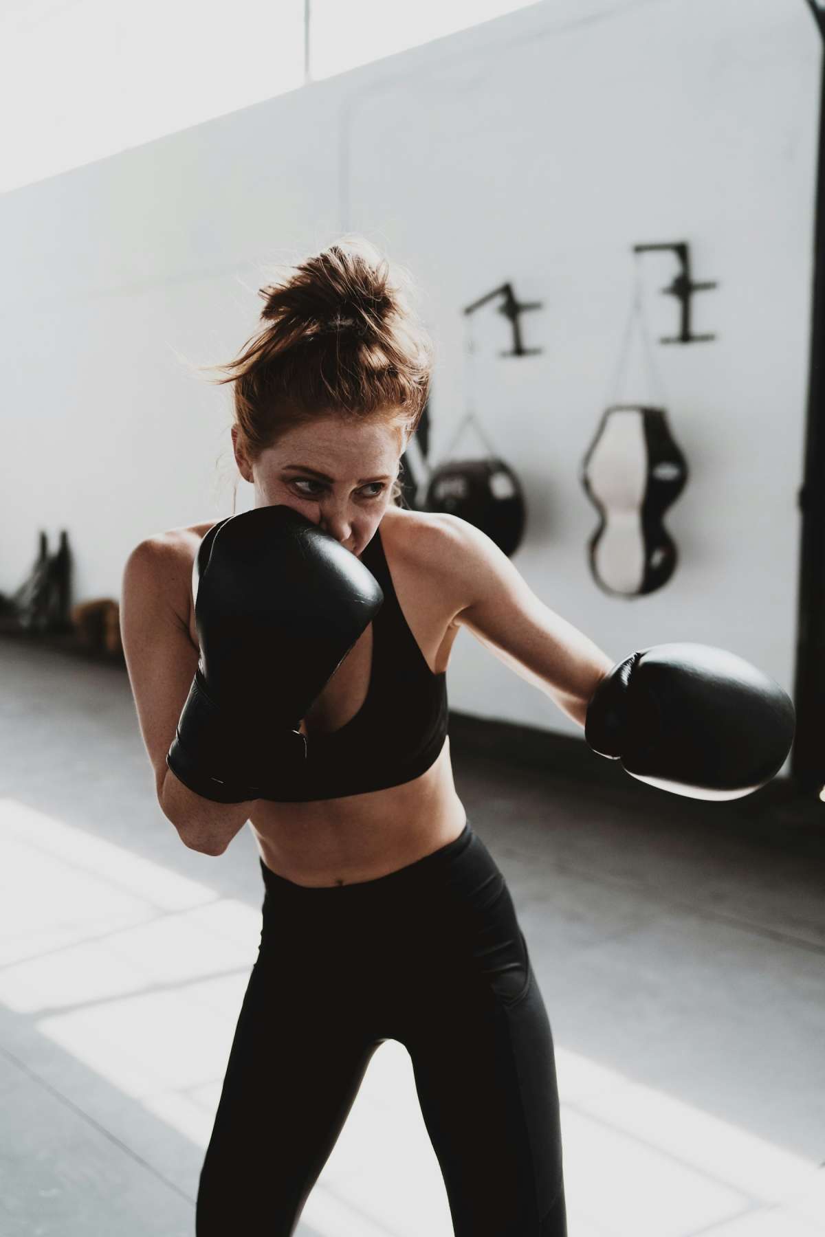 Woman in black sports bra, leggings and boxing gloves throwing a punch in a bright gym