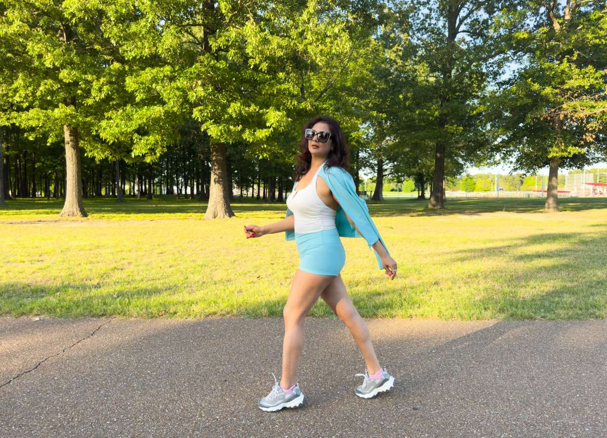 Woman in light blue activewear and grey walking sneakers striding along a paved park path